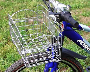 A galvanized grid style bicycle basket is mounted on the handlebar of a mountain bike