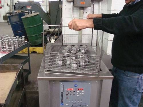 A man is holding the handle of ultrasonic industrial cleaning baskets and several parts in it.